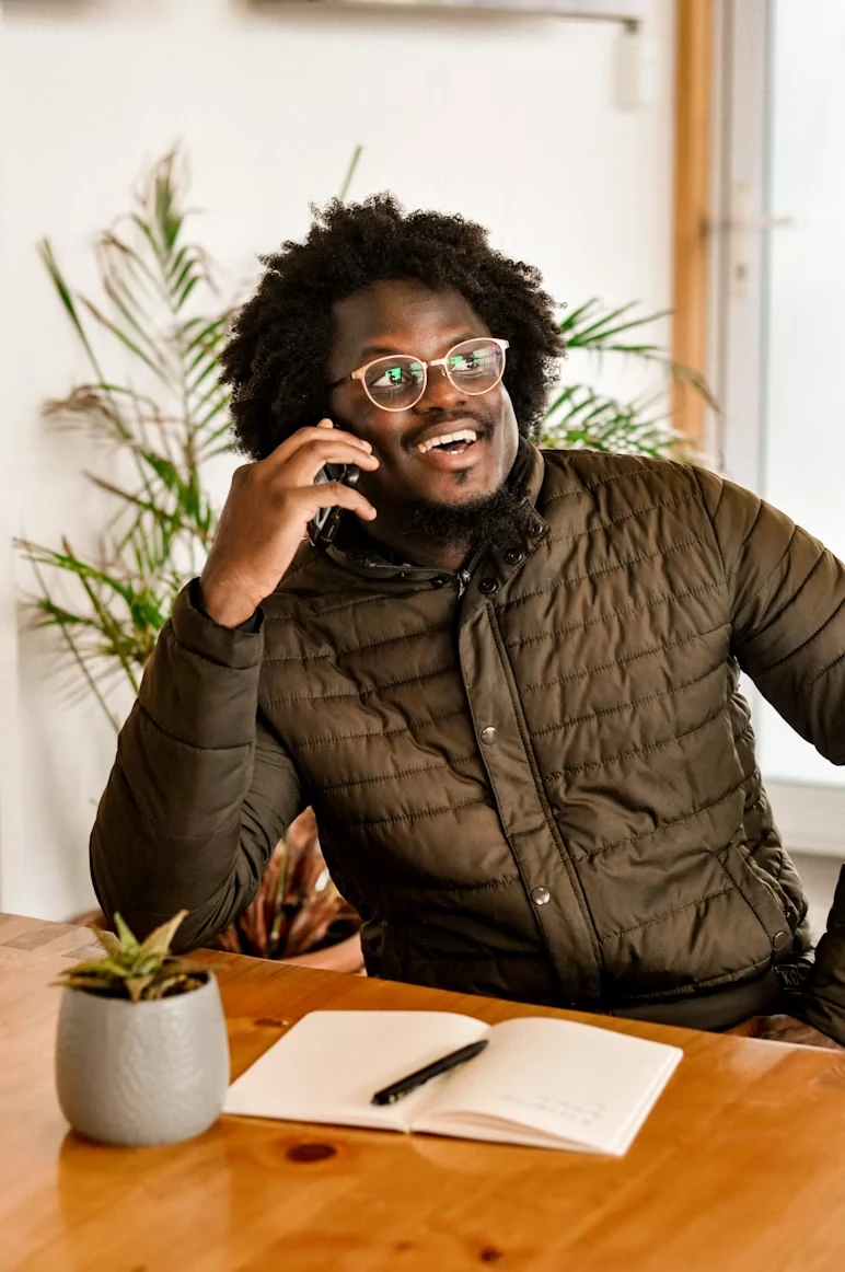 A client smiling while on a phone call at a desk, taking notes in a notebook